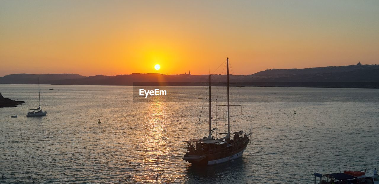 Sailboats moored on sea against sky during sunset