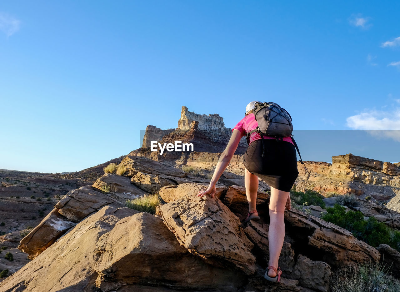Rear view of woman climbing on rock against clear blue sky