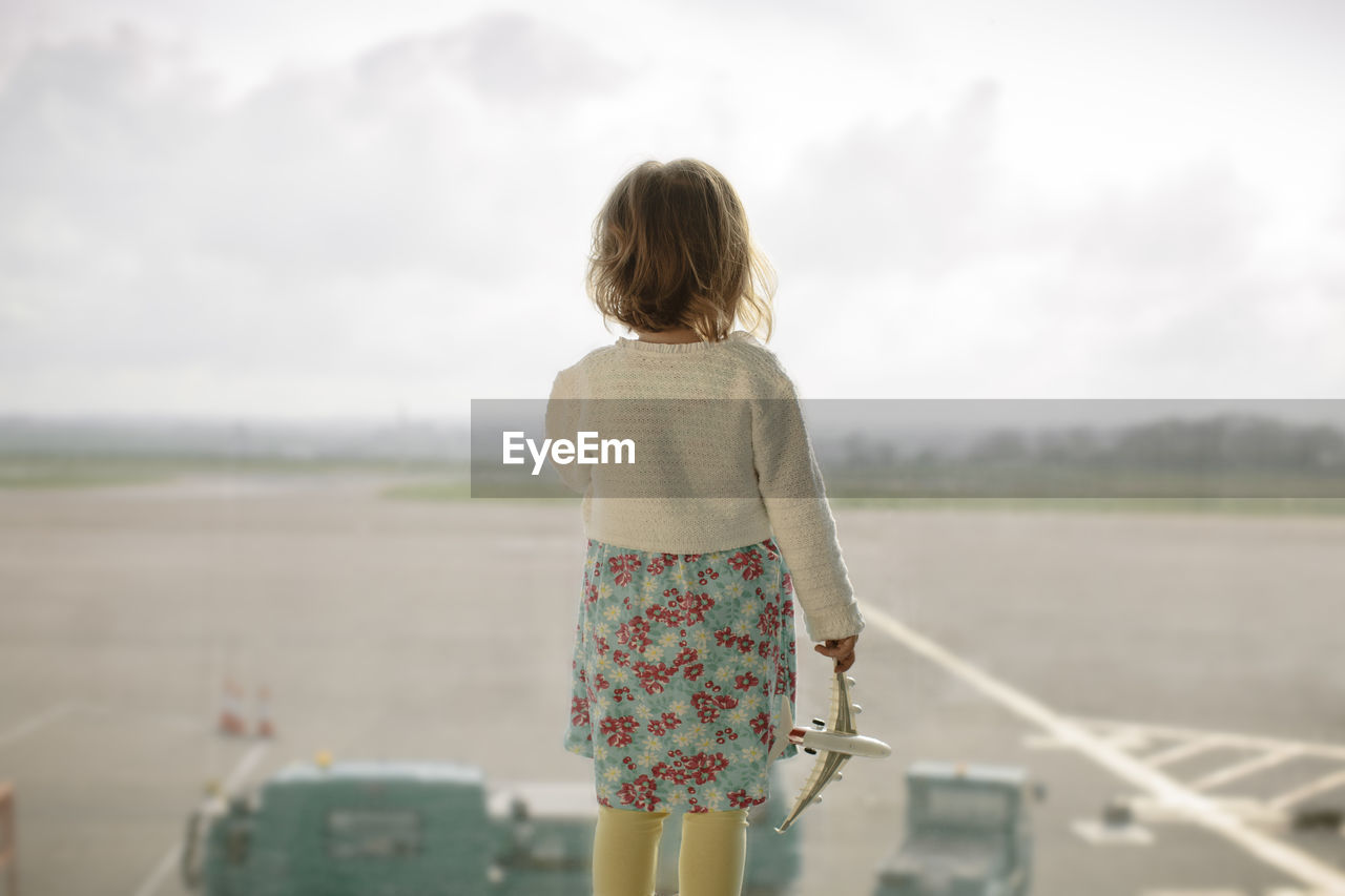 Rear view of child looking at airport runway against sky