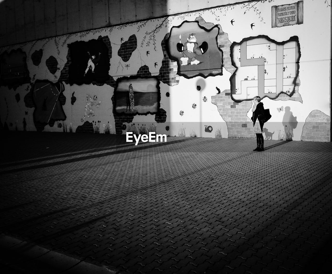 Woman looking away while standing on footpath against wall