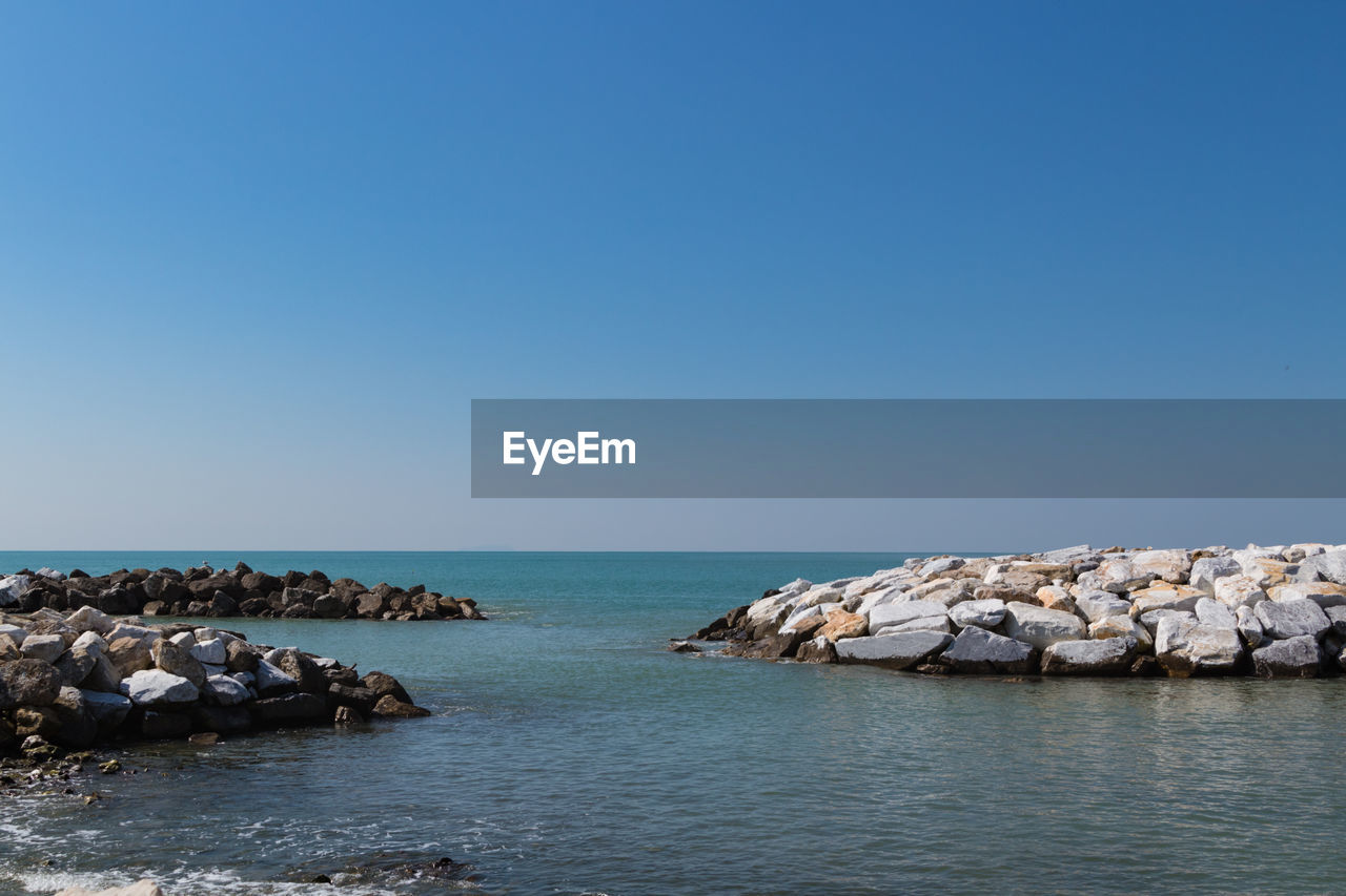 ROCKS IN SEA AGAINST CLEAR BLUE SKY