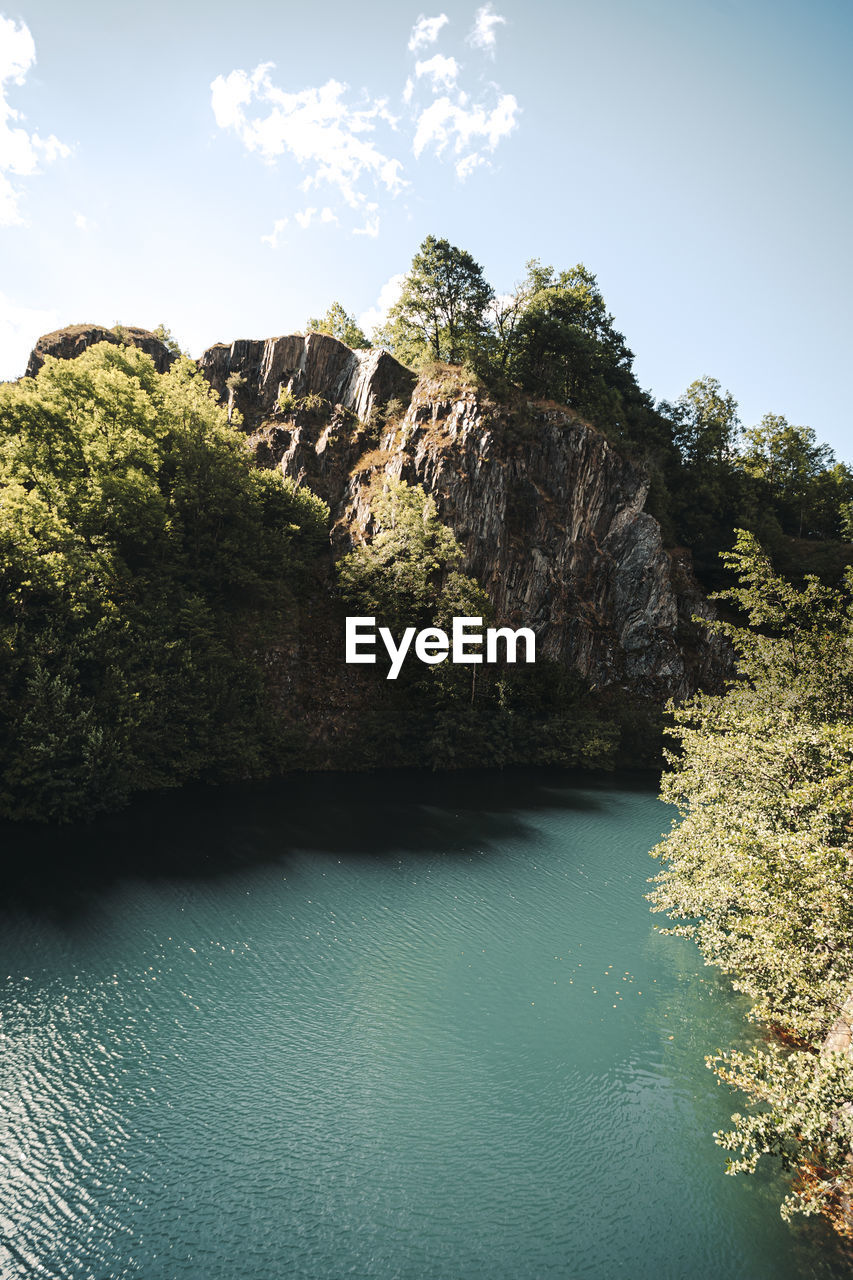 Scenic view of cliff by trees against sky