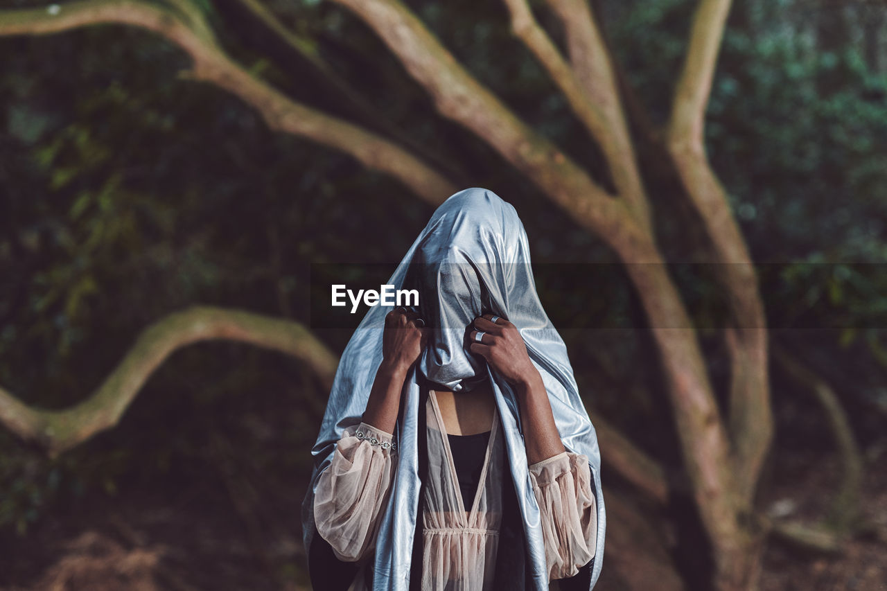 Close-up of woman with textile on face standing against tree