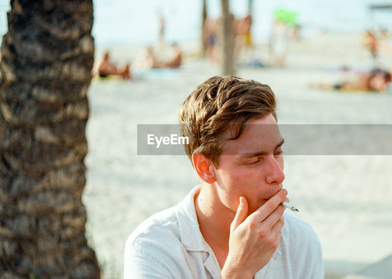 Young man smoking cigarette at beach