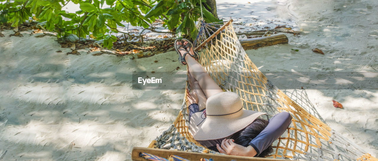 Tourist laying on beach swing, covering face with hat, holiday sunbathing on beach, phangnga