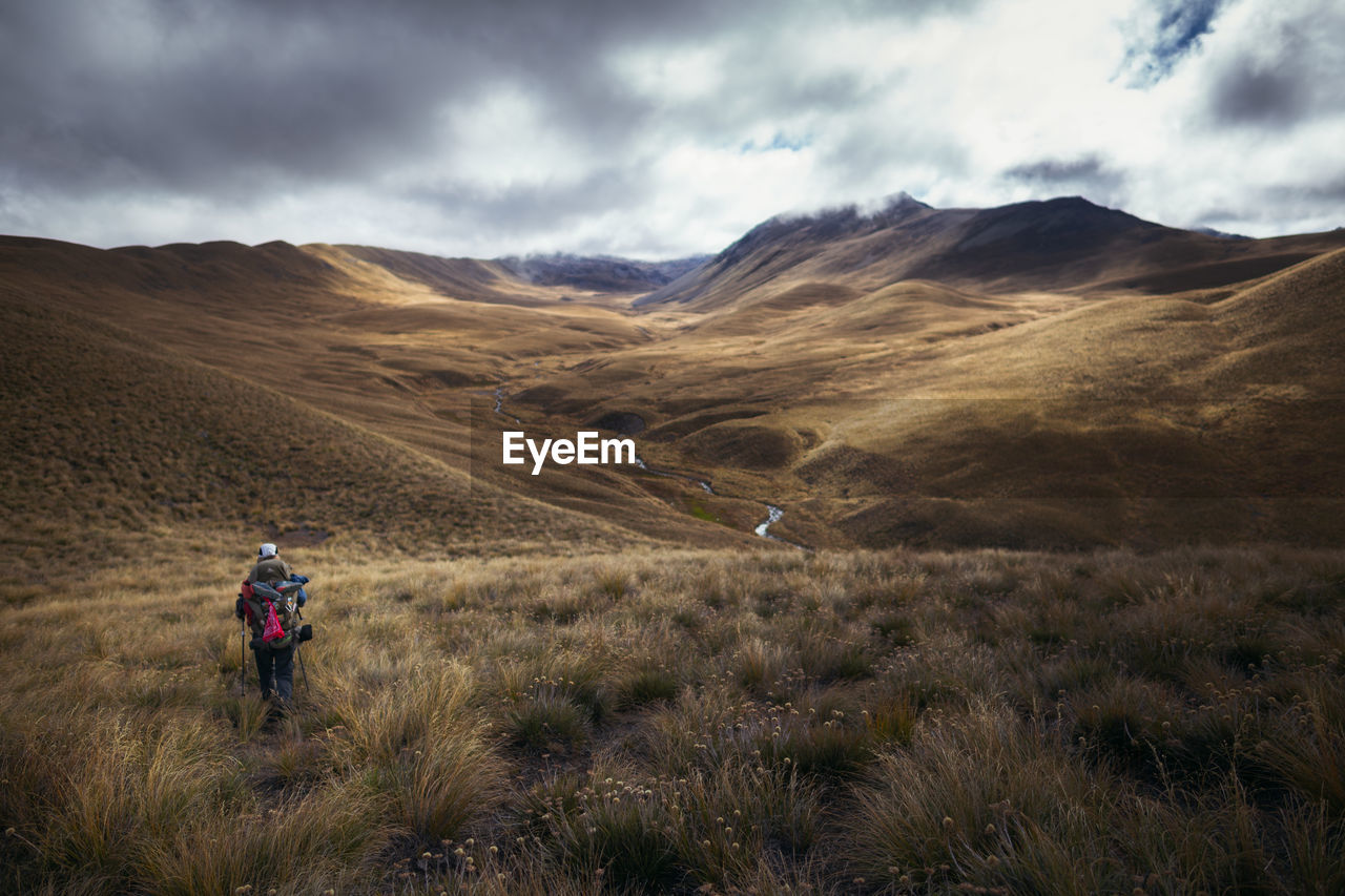 Rear view of woman walking on field against mountain and sky