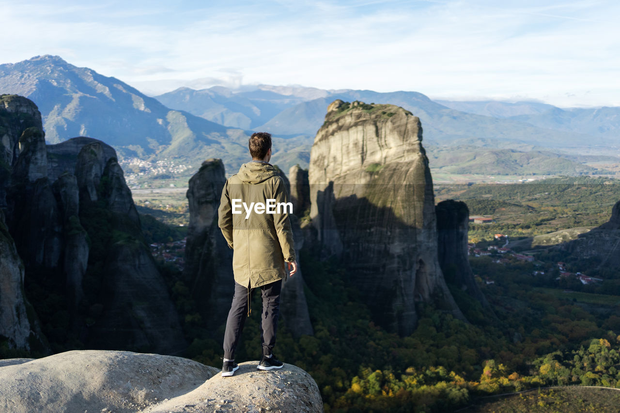 Rear view of man standing on rocks against mountains