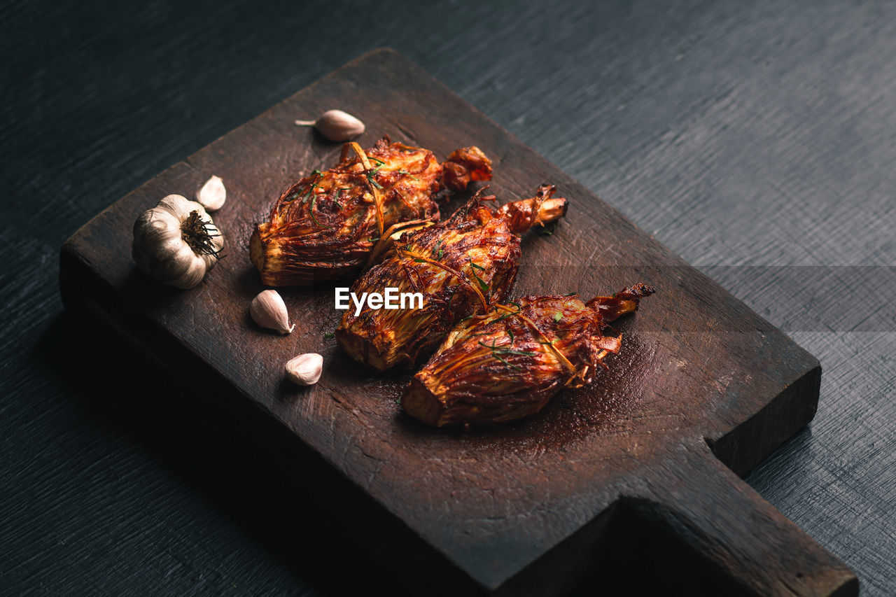 High angle view of chicken meat with garlic cloves served on wooden tray