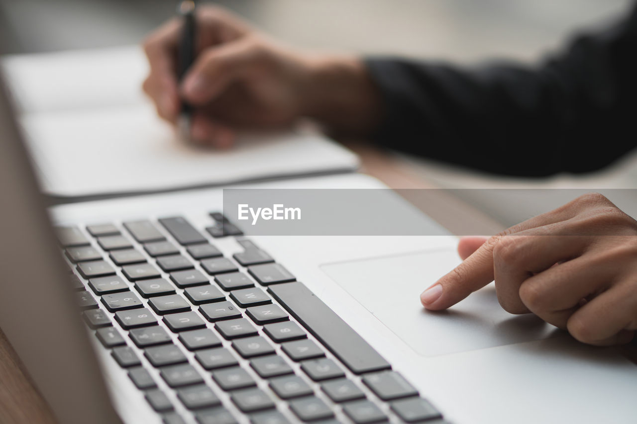 cropped hands of man using laptop at table