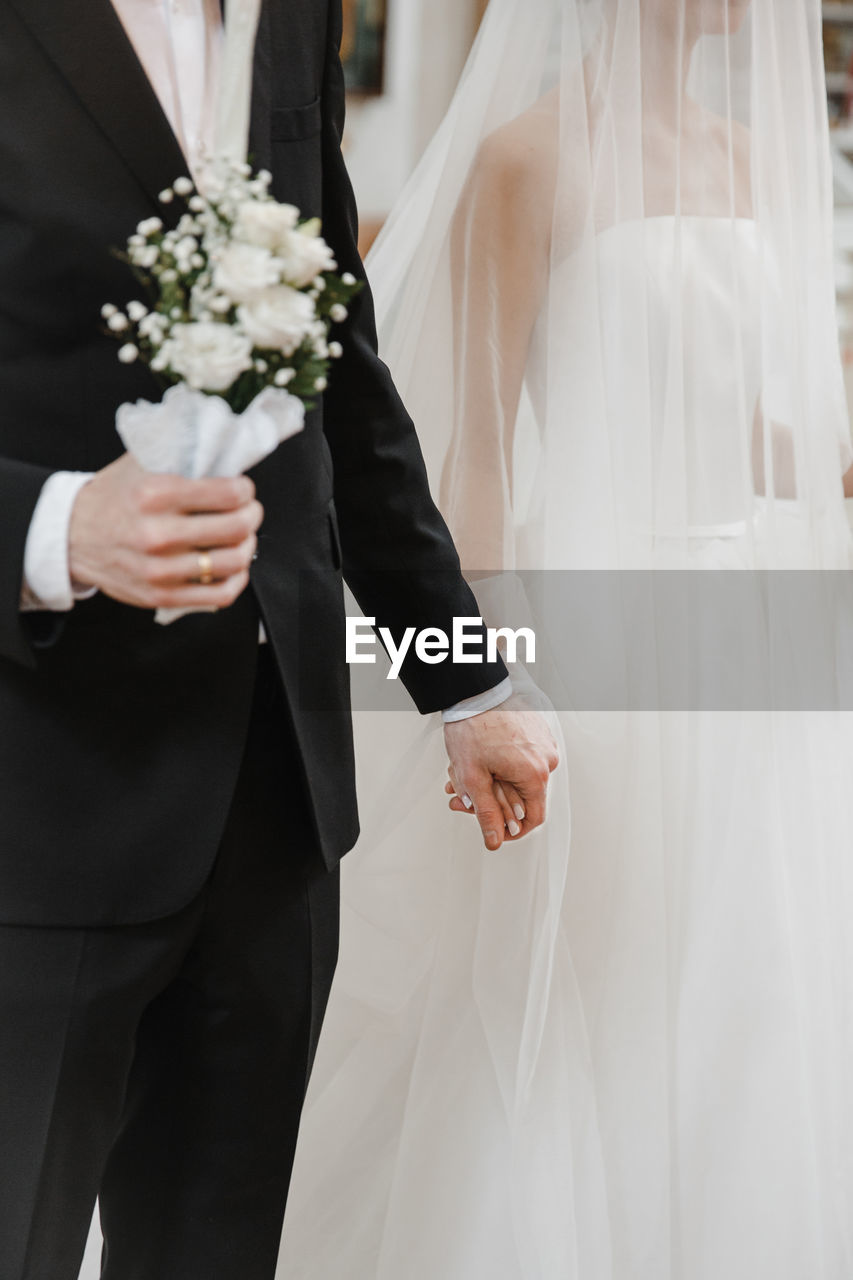 midsection of bride and bridegroom holding bouquet