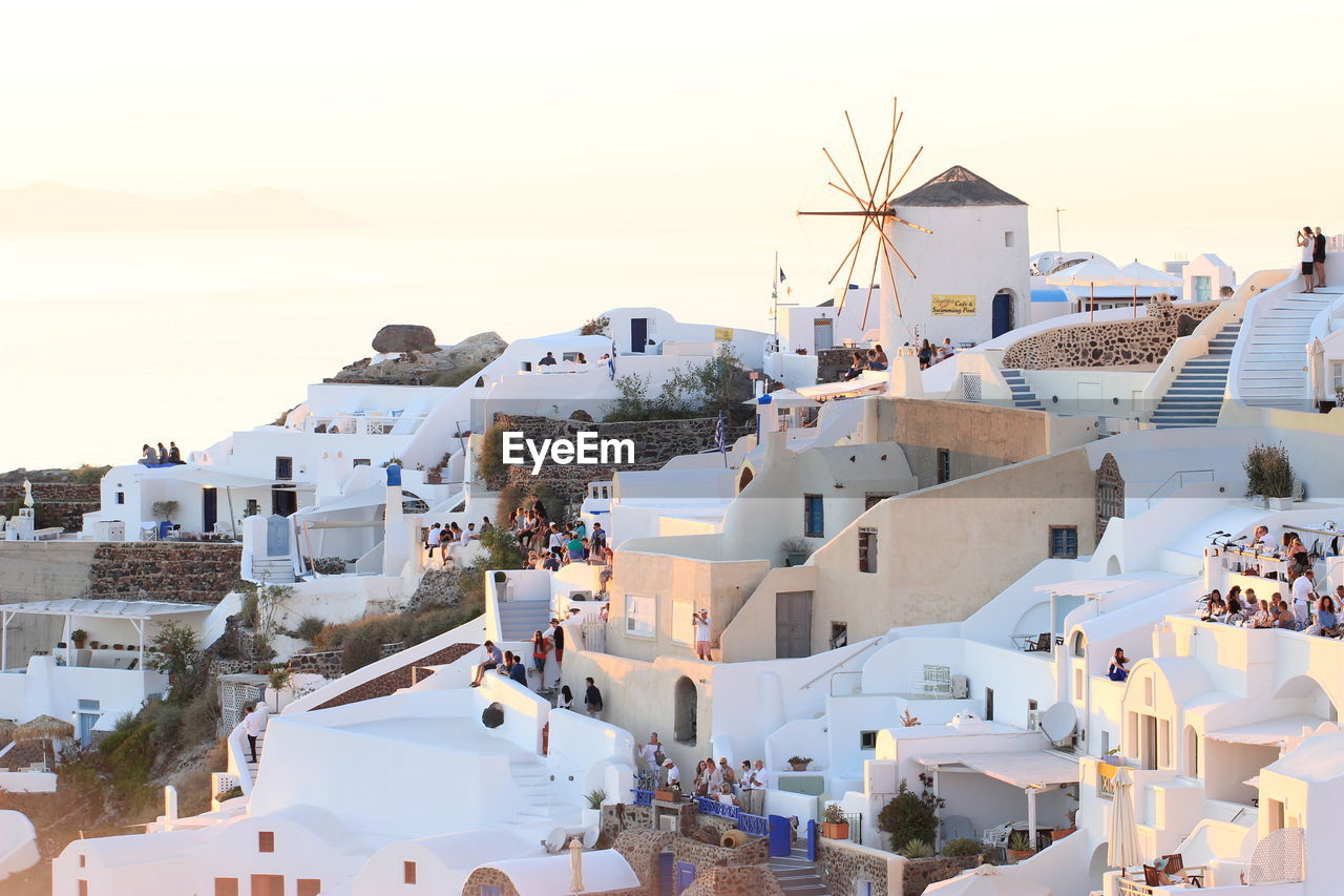 Tourists visiting village at santorini against clear sky during sunset