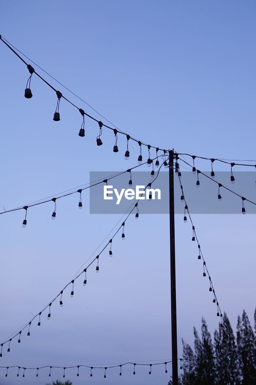 Low angle view of birds perching on cable against sky