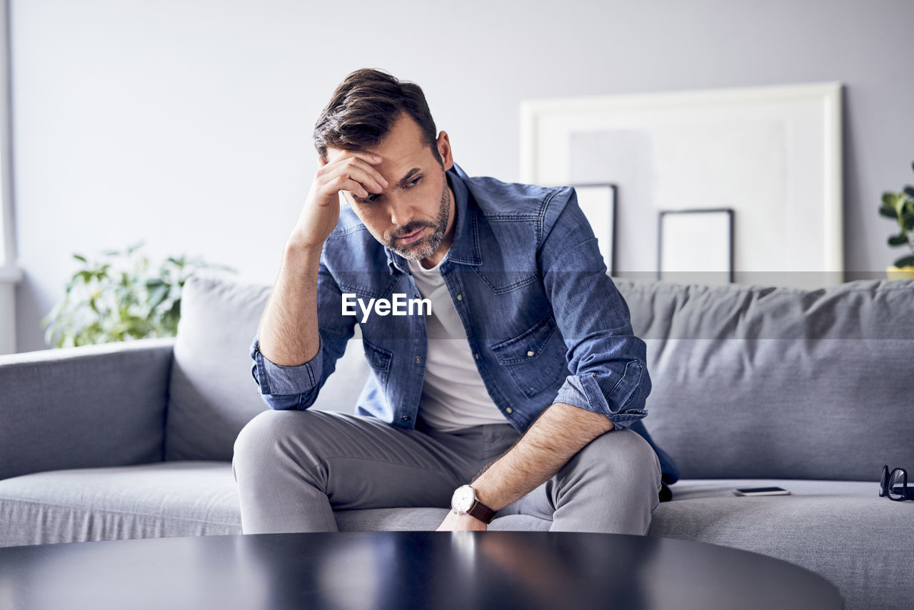 Worried thoughtful man sitting on sofa