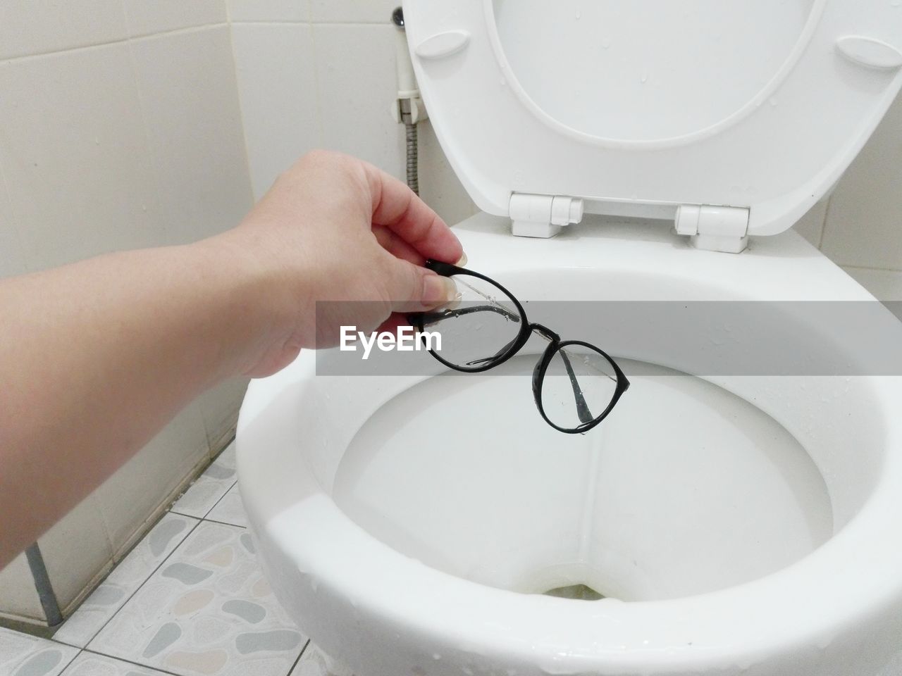 Cropped hand of woman putting eyeglasses in toilet bowl