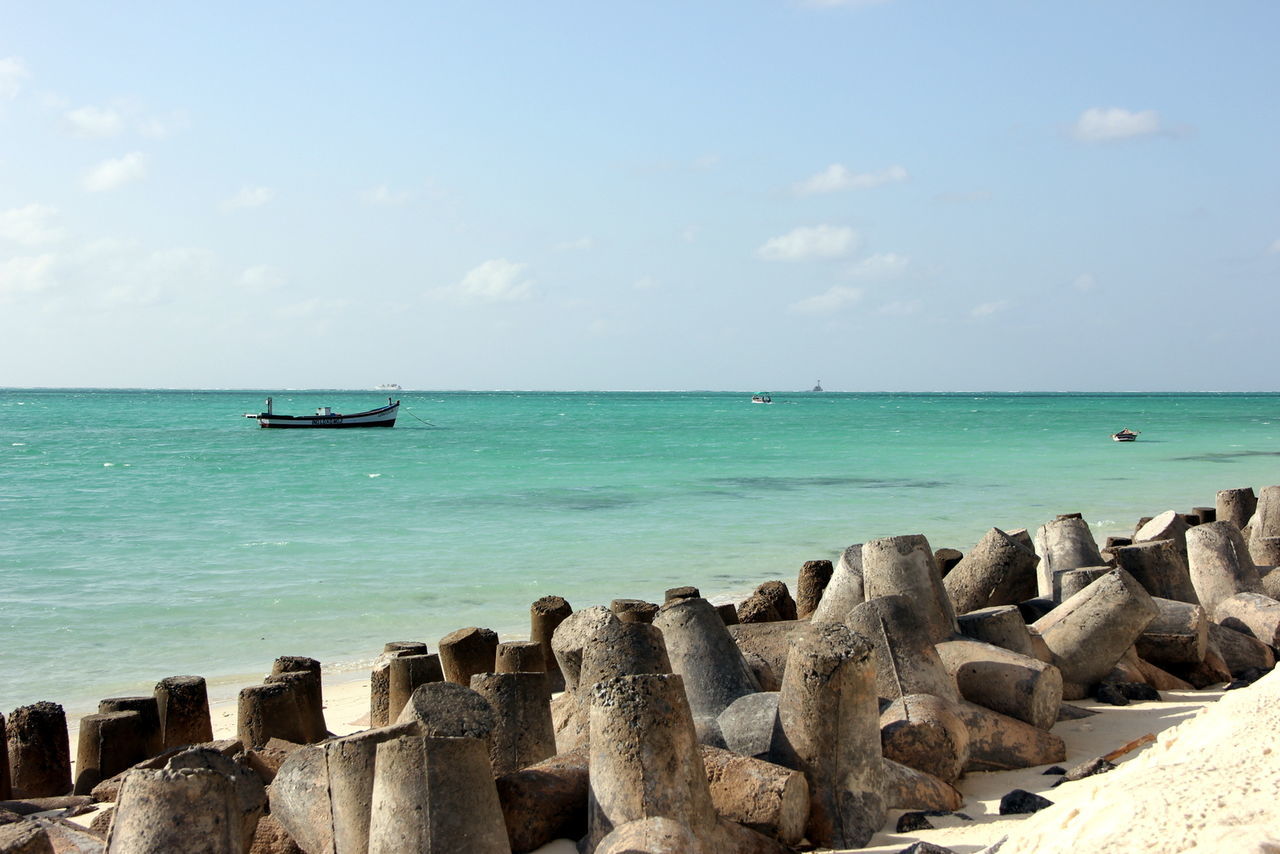 Scenic view of boat in sea with groyne on shore against sky