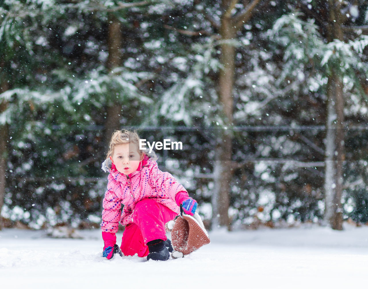 Young girl child kneeling in snow storm during light flurries in winter