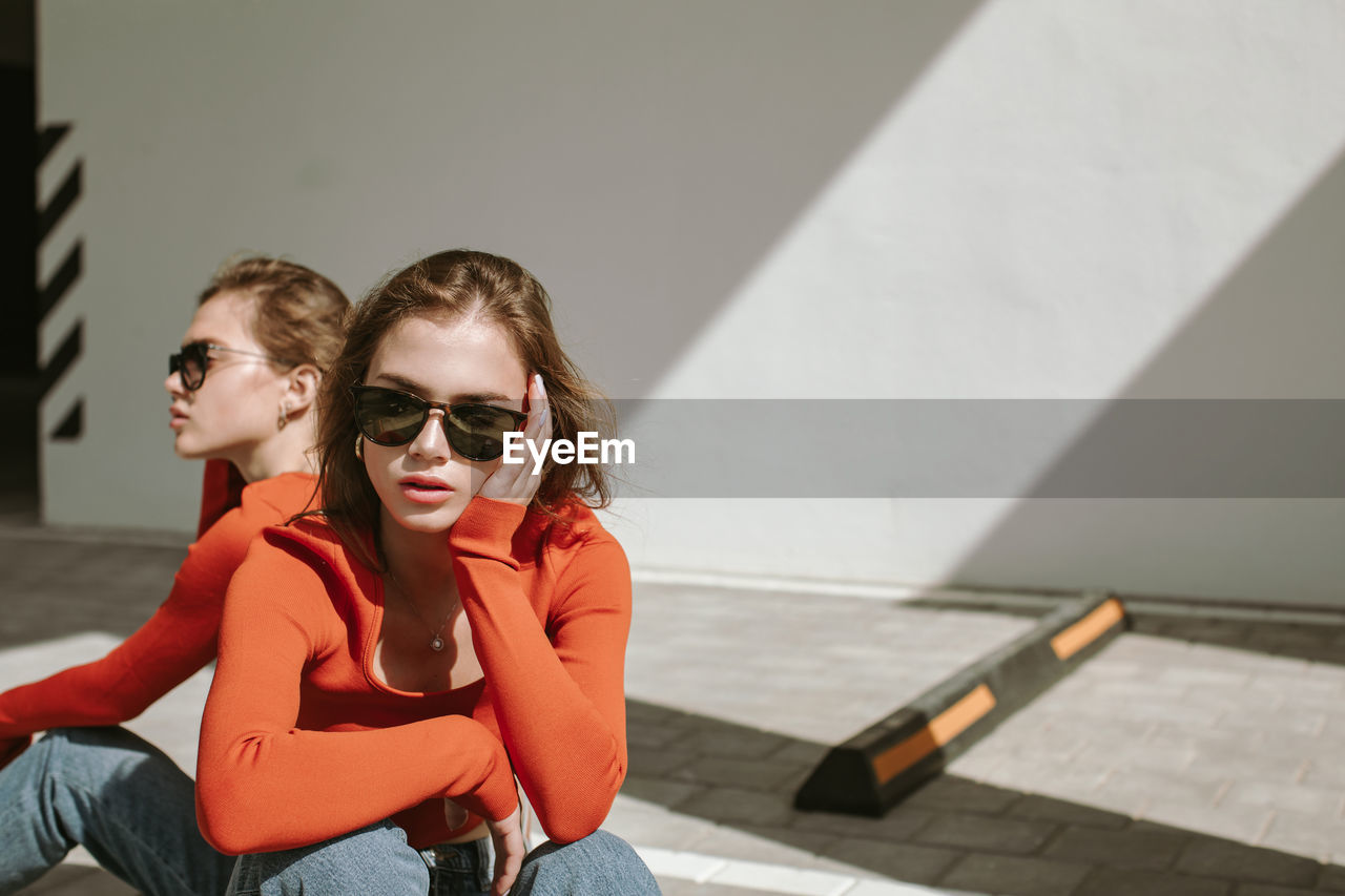 Portrait of two young girls in sunglasses and identical clothes posing in urban area. copy space.