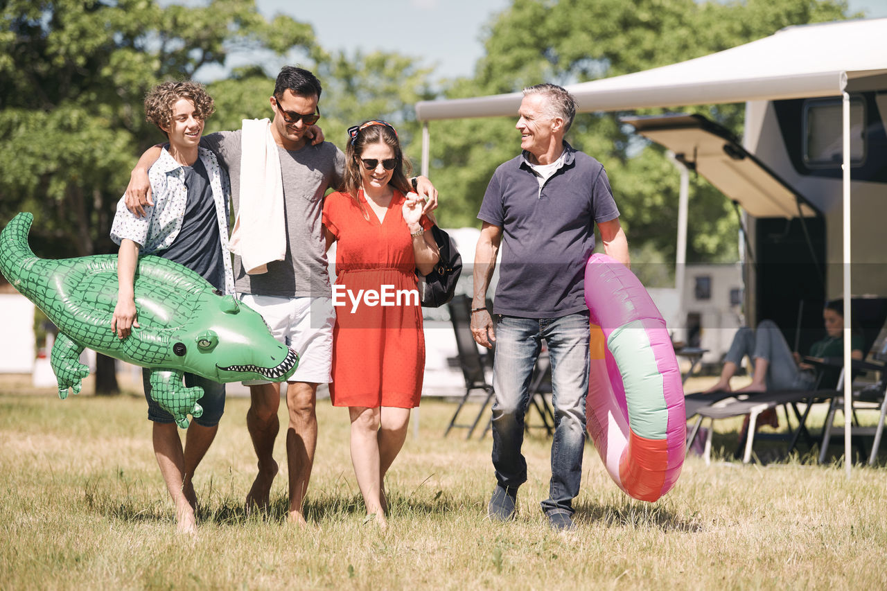 Happy family with inflatable rings walking on grassy field by travel trailers