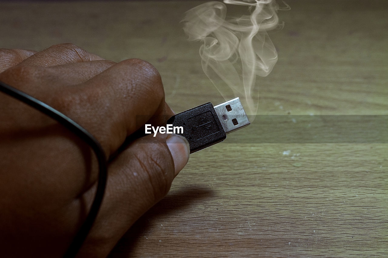 CLOSE-UP OF PERSON HAND HOLDING CIGARETTE AND TEXT ON TABLE