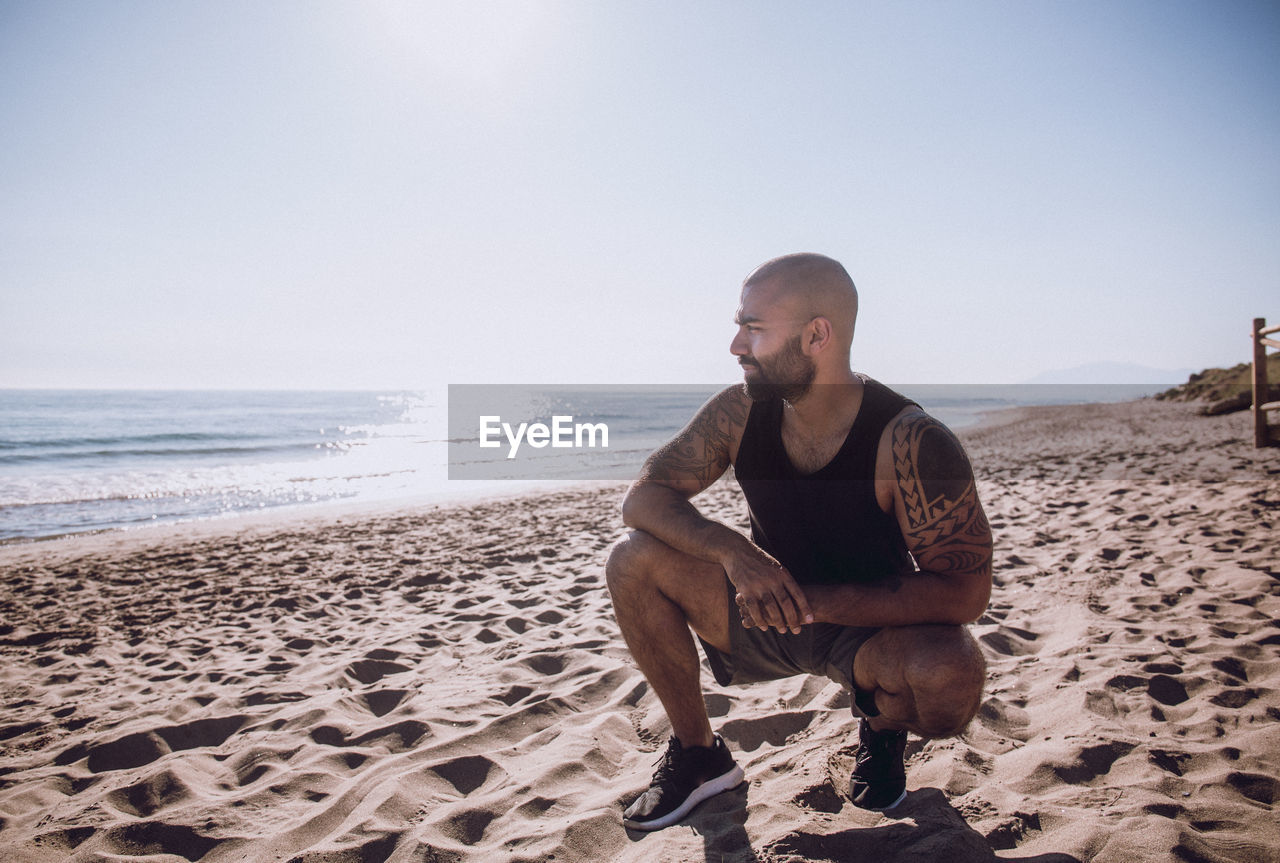 Full length of man crouching at beach against sky