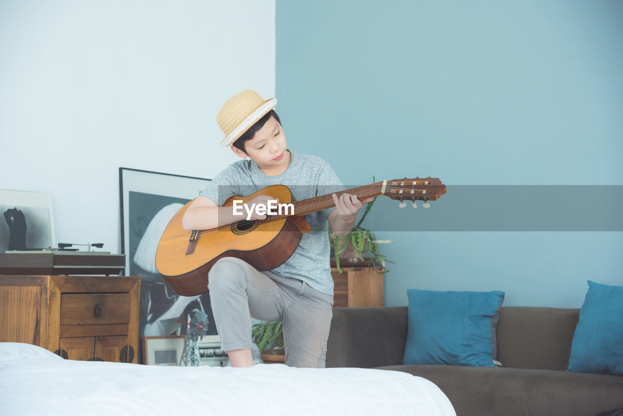 Boy playing guitar while standing at home