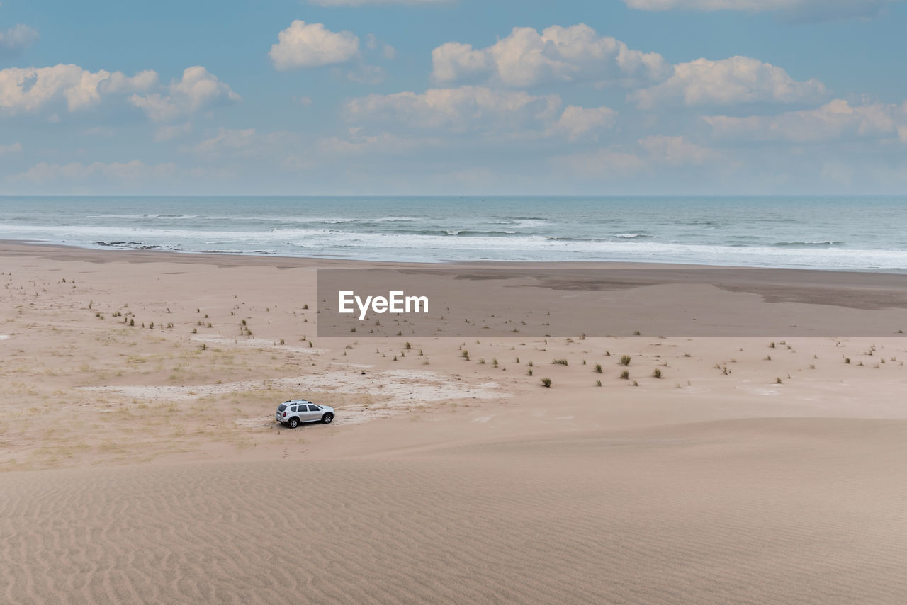 View of a vehicle in the dunes. behind more dunes, the sea and the cloudy sky.