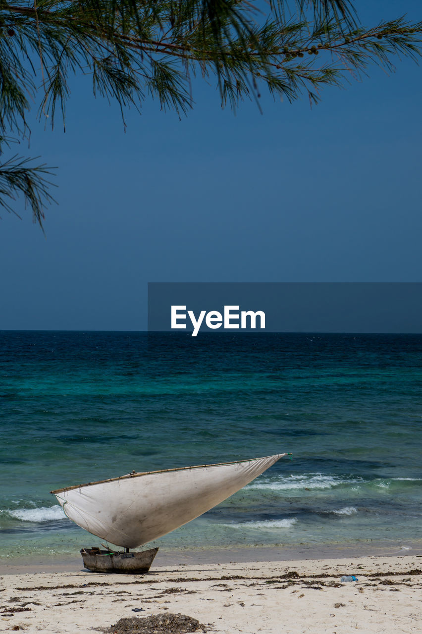 Boat moored at beach against clear blue sky