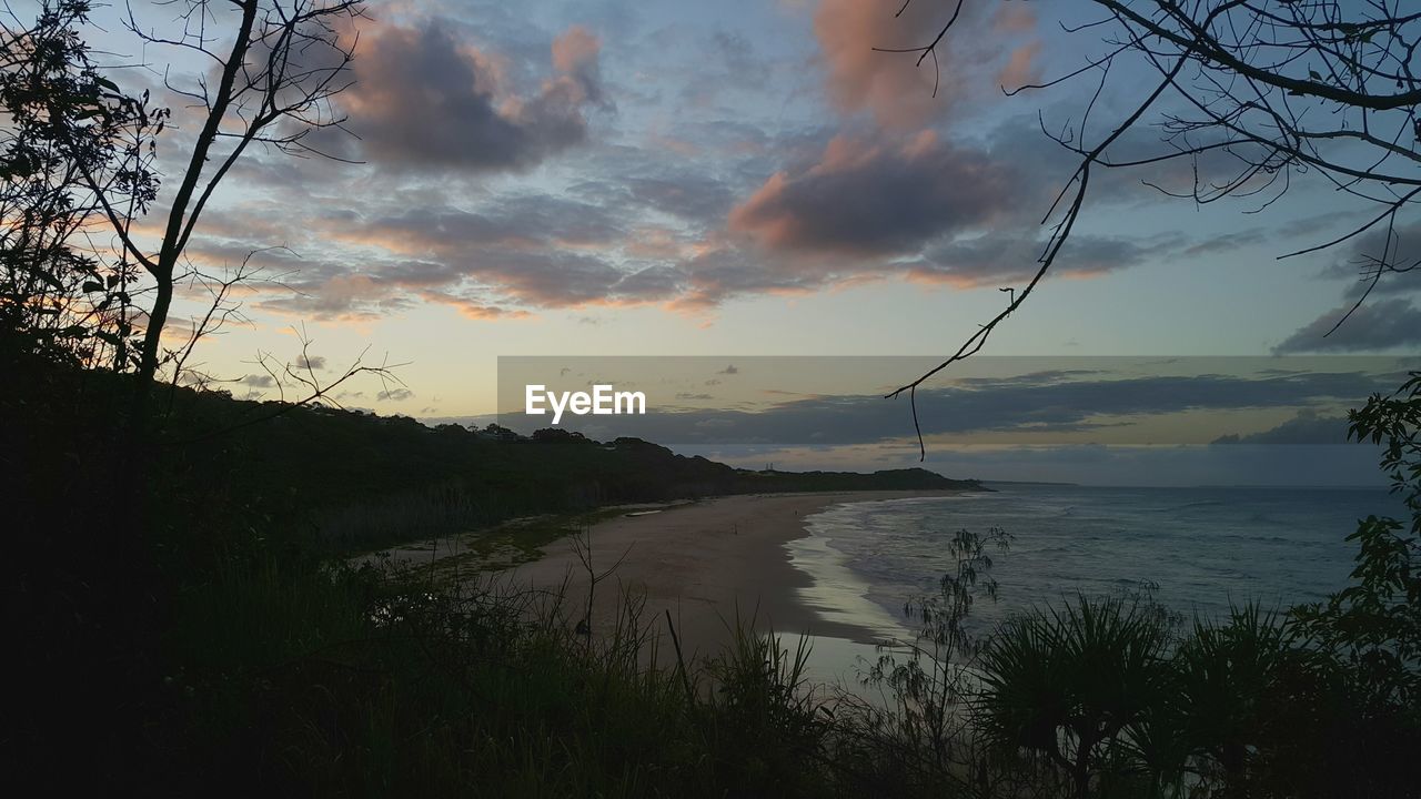 Scenic view of sea by mountain against sky during sunset