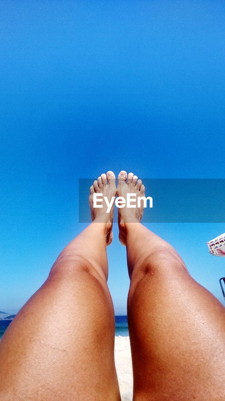 Low section of woman feet up against clear blue sky