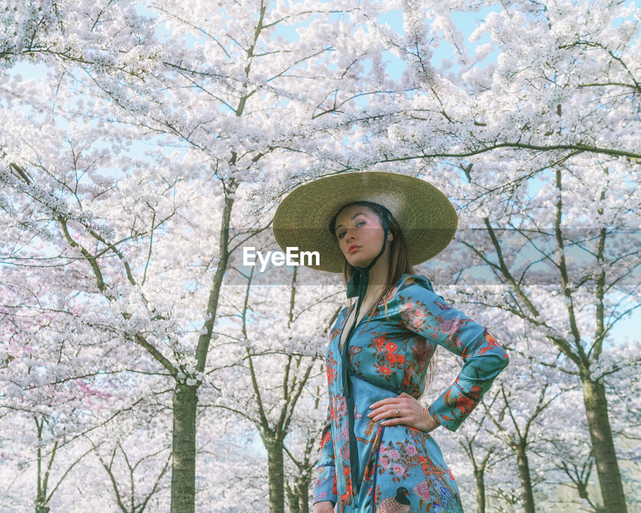 Low angle view of woman wearing hat standing against blooming trees