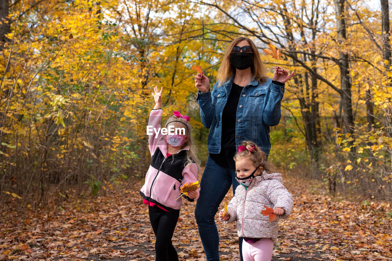 Mother with daughters wearing mask standing in forest during autumn