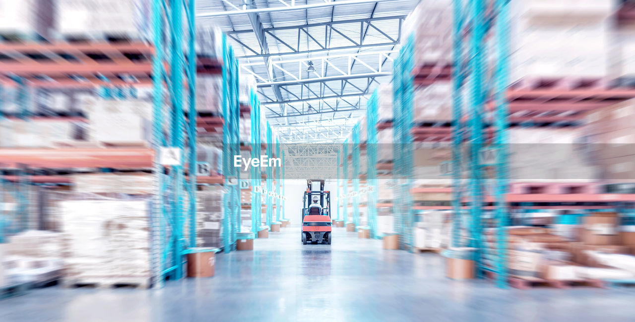 Warehouse metal structure interior with forklift truck in selective focus, rows of merchandise