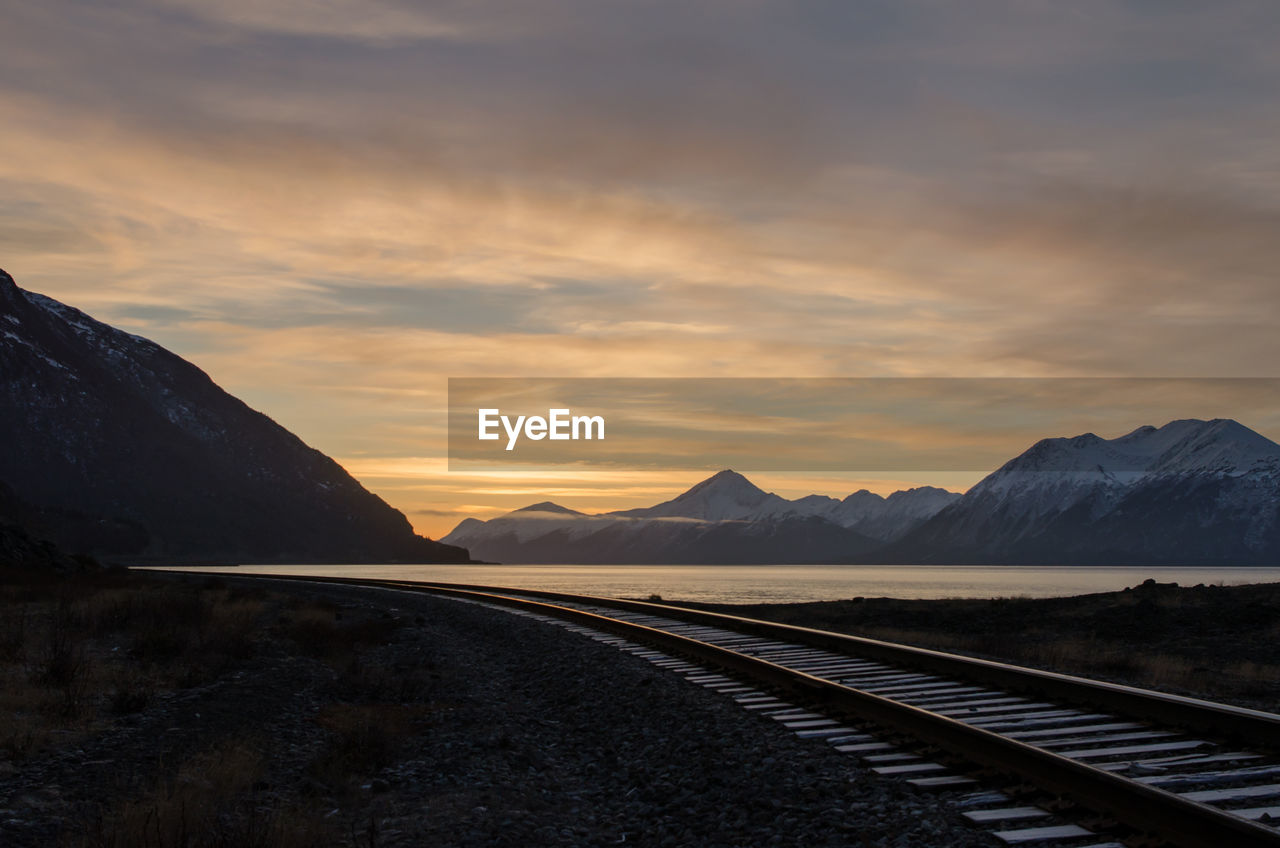 View of railroad track by lake at sunset