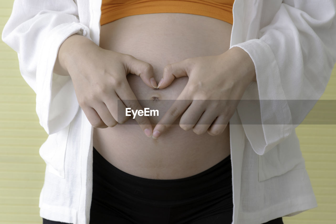 MIDSECTION OF WOMAN TOUCHING MIRROR AGAINST WALL