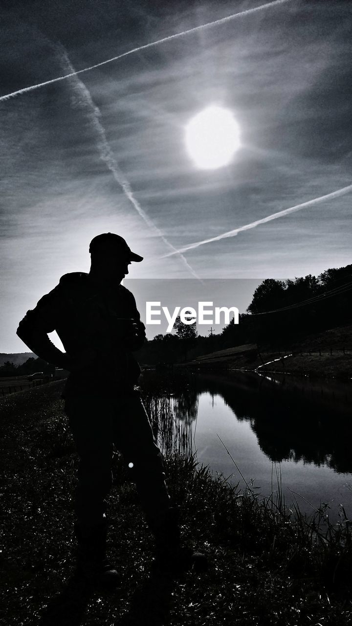 SILHOUETTE OF MAN STANDING BY LAKE AGAINST SKY