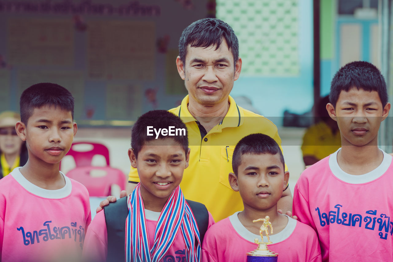 PORTRAIT OF A SMILING BOY WITH PEOPLE IN THE BACKGROUND