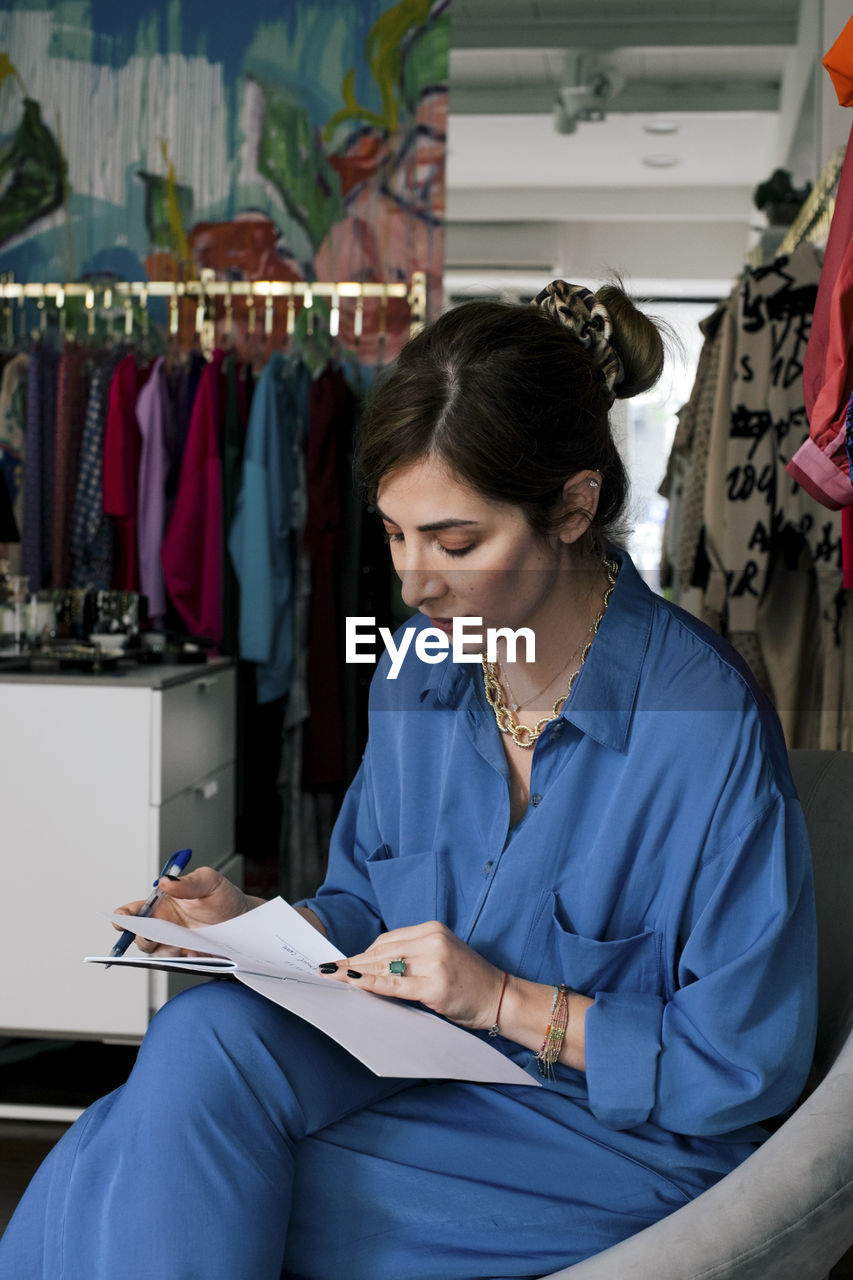 Female owner reading book while sitting in clothing store