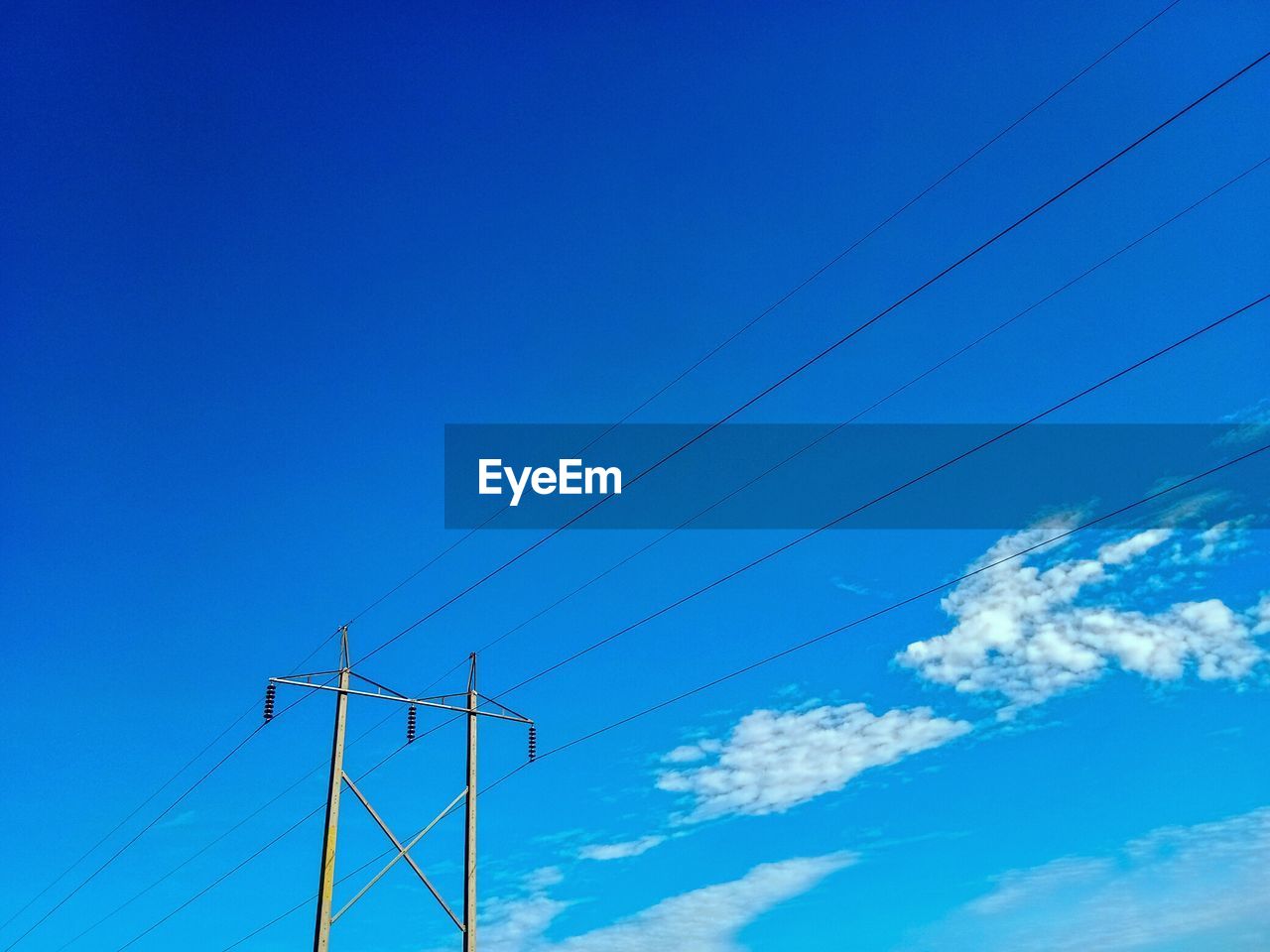 Low angle view of electricity pylon against blue sky