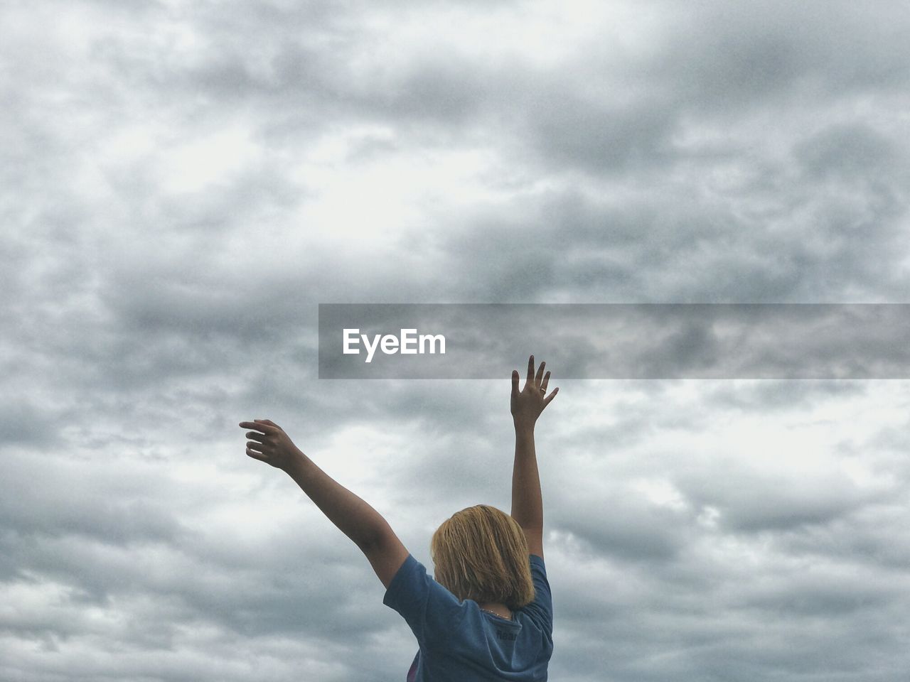 Low angle view of woman with arms raised against cloudy sky