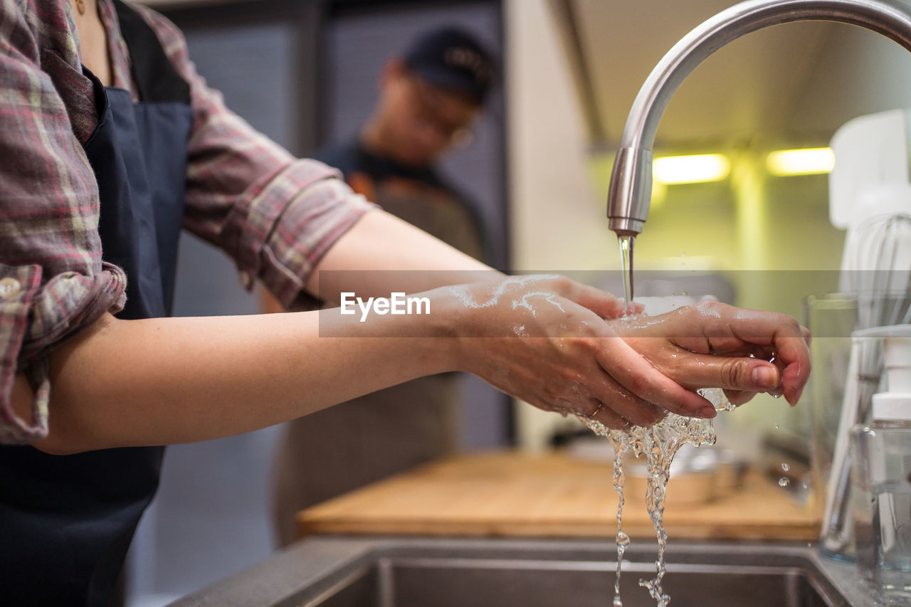 Cropped side view of woman washing hands in sink while having home bakery with man