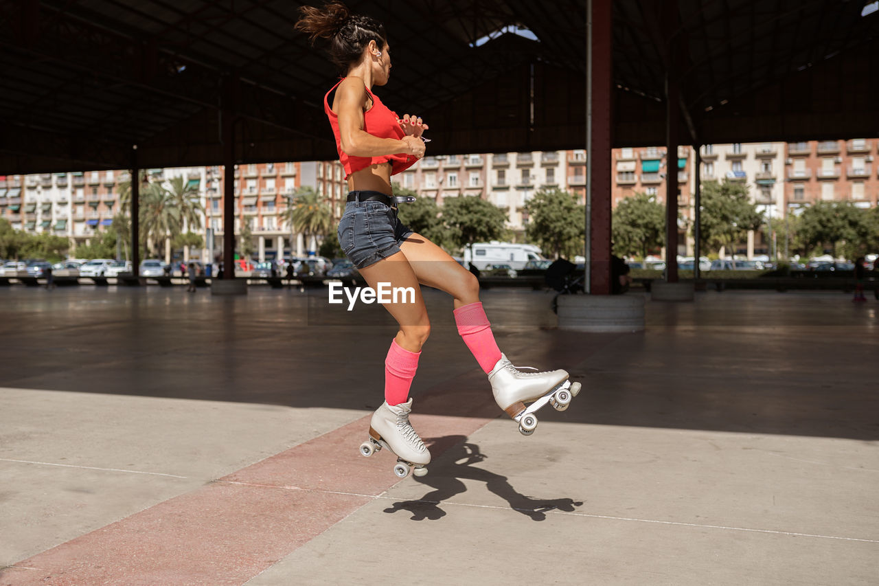 Concentrated female balancing on leg while roller skating on sports ground on sunny day in city