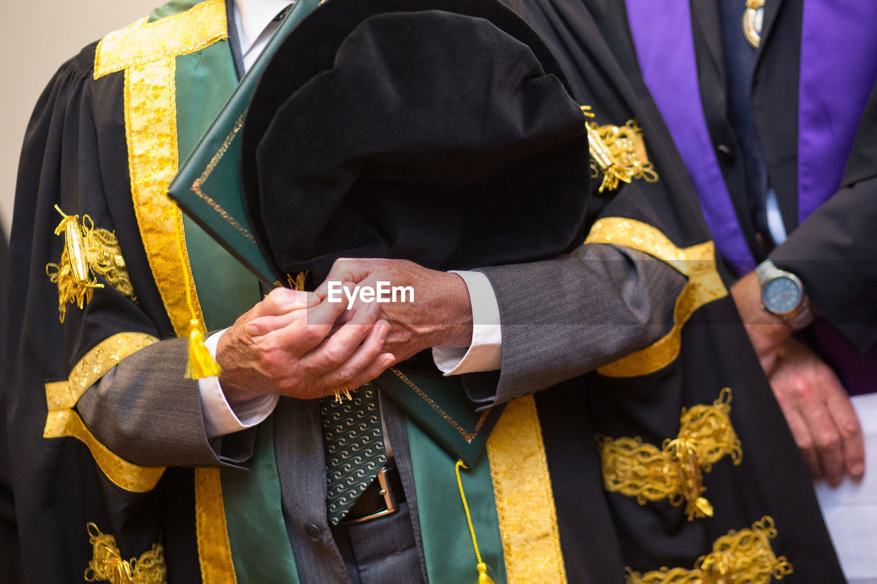 Midsection of man with certificate wearing gown during graduation ceremony