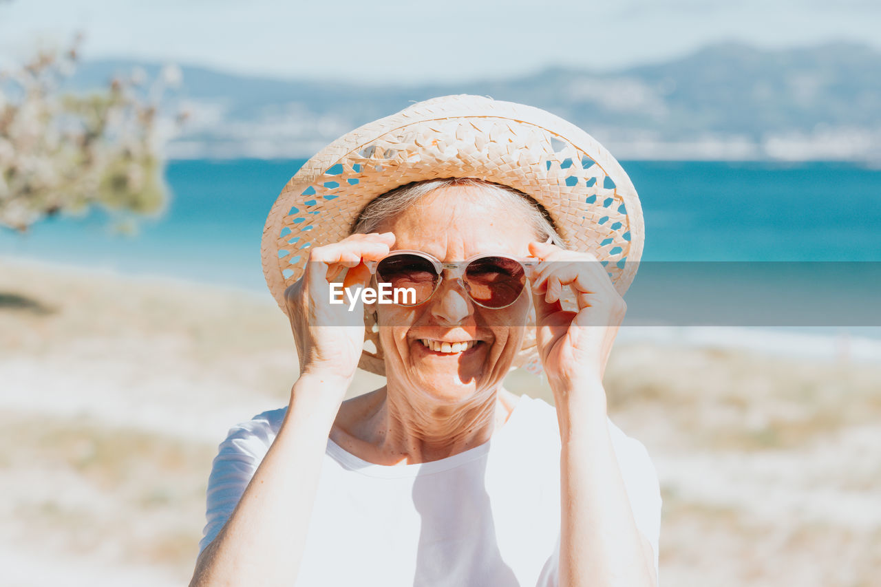 portrait of young woman wearing sunglasses while standing at beach