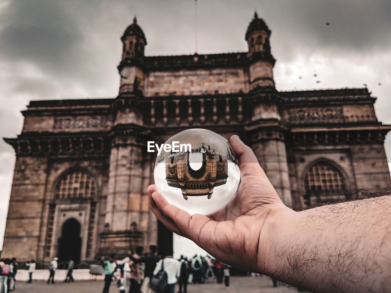 Cropped hand holding crystal ball with gateway of india reflection