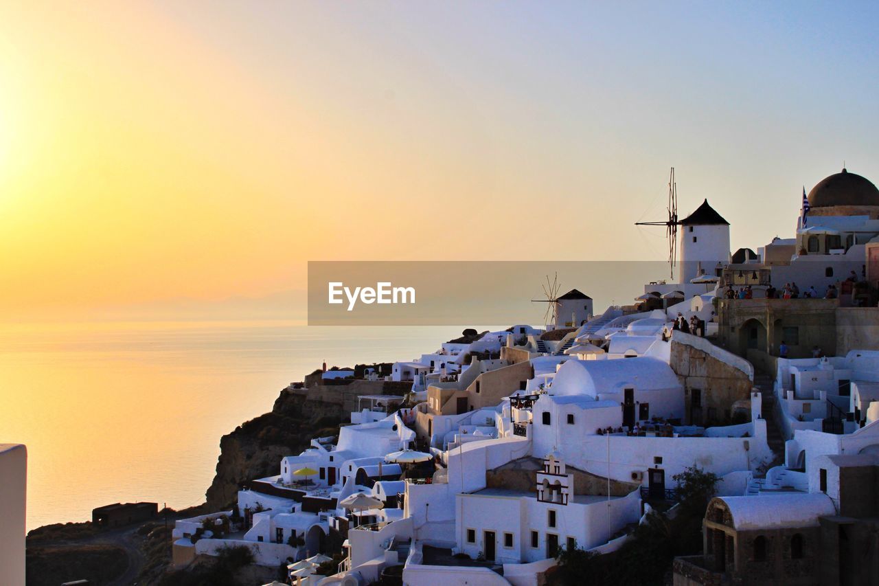 Traditional windmills amidst houses at santorini against sky during sunset