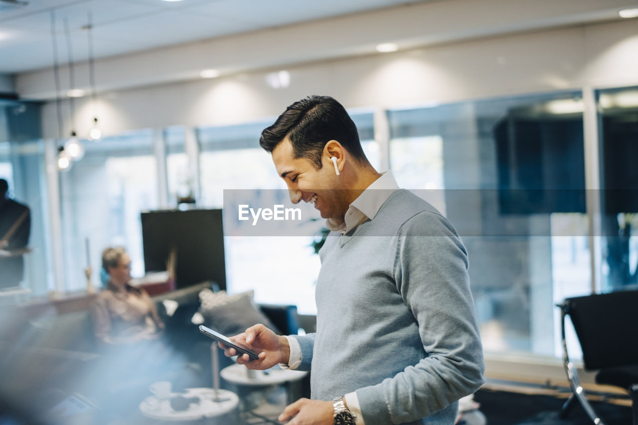 Businessman laughing while text messaging on smart phone at office