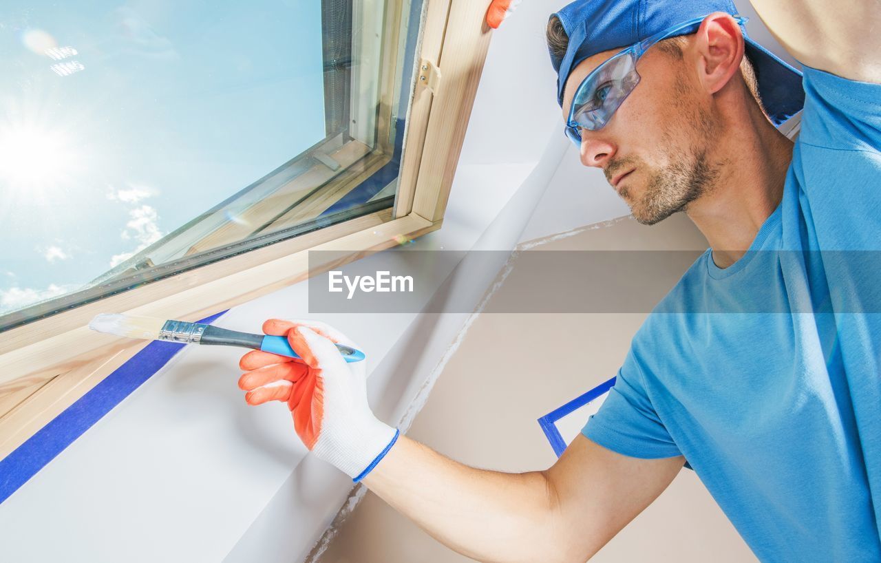 Low angle view of painter painting window at home