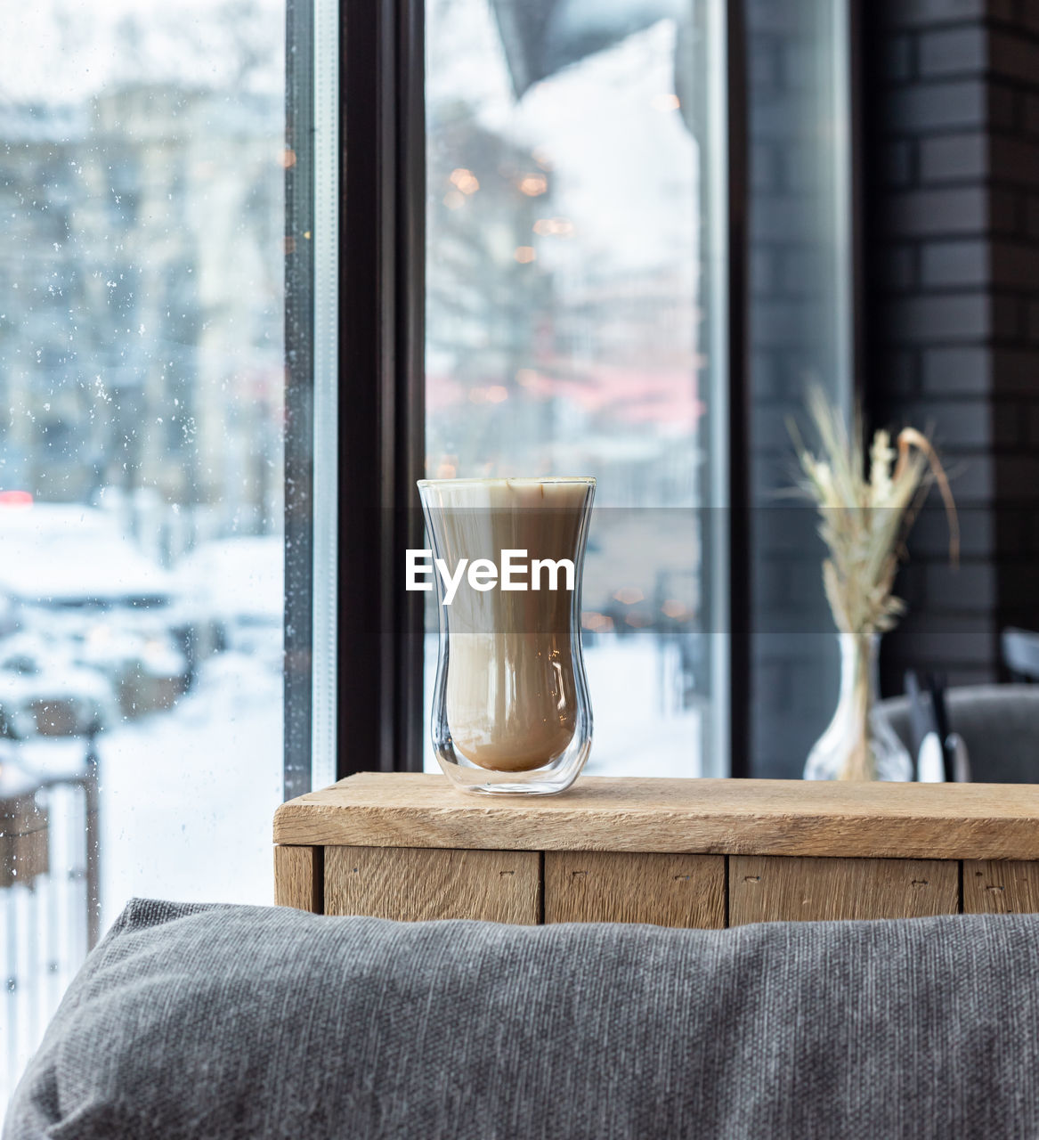 Coffee with milk foam in glass cup on wooden table in cafe or coffeehouse.