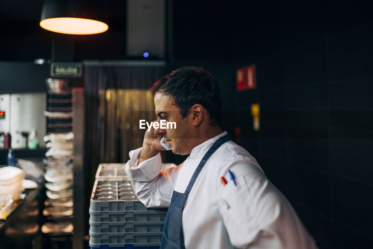 Side view of man working in restaurant kitchen and having phone call