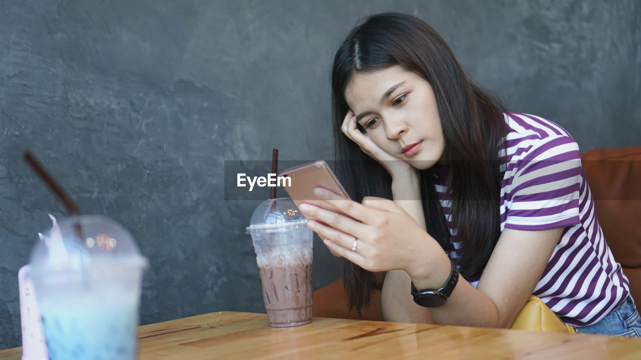 Young woman using smart phone sitting at table with coffee in cafe 